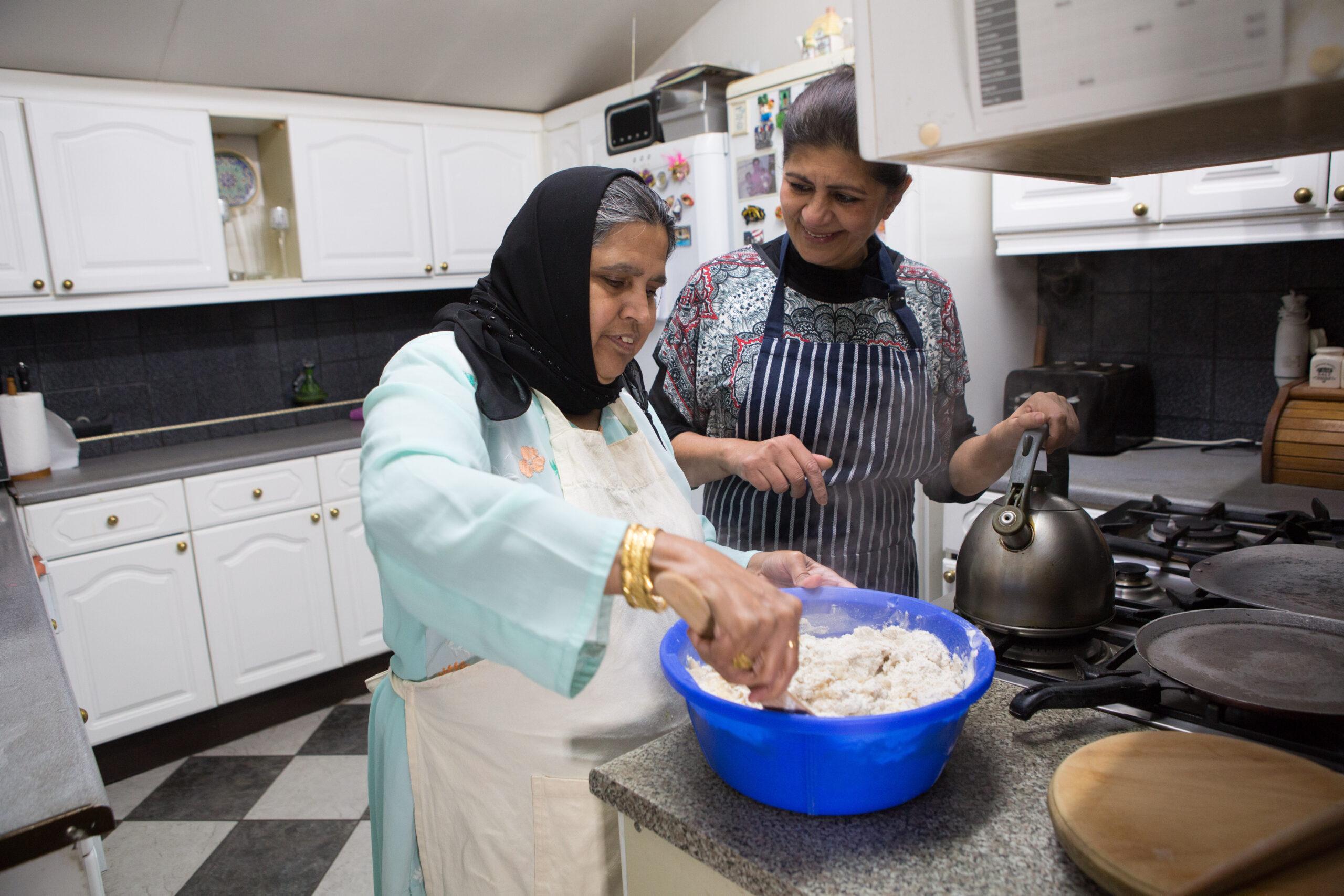 A carer helping a woman cooking in the kitchen.