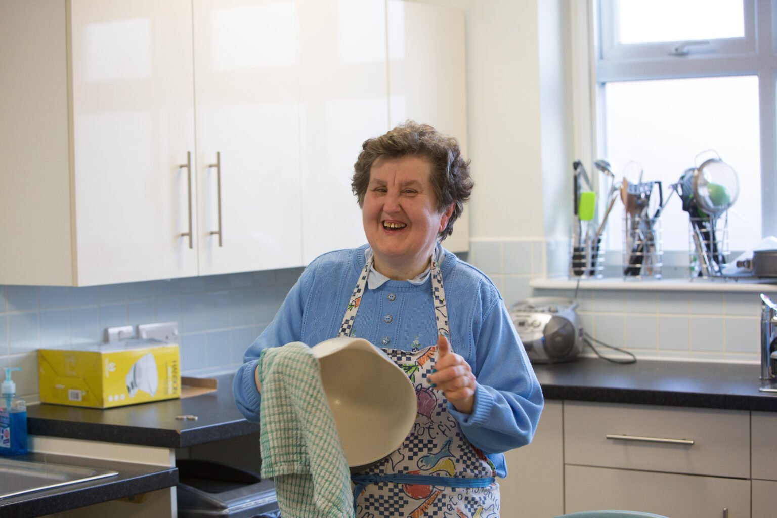 older lady in the kitchen, drying a bowl and smiling