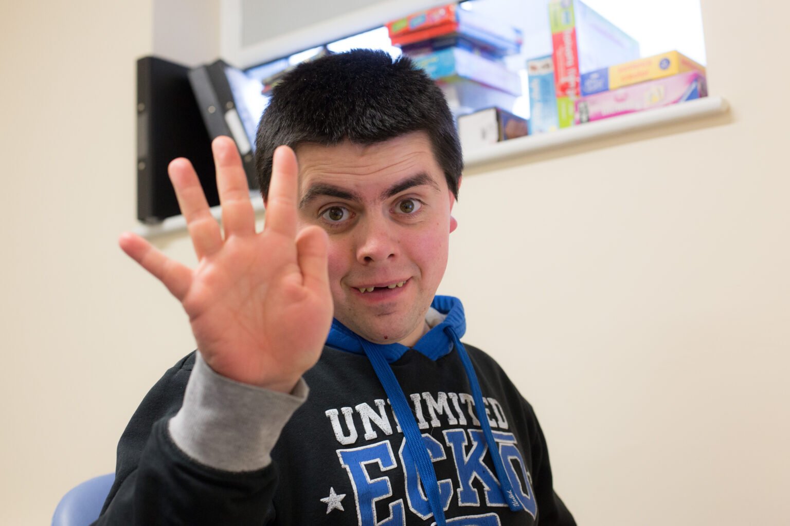 young man with down syndrome smiling and waving to the camera