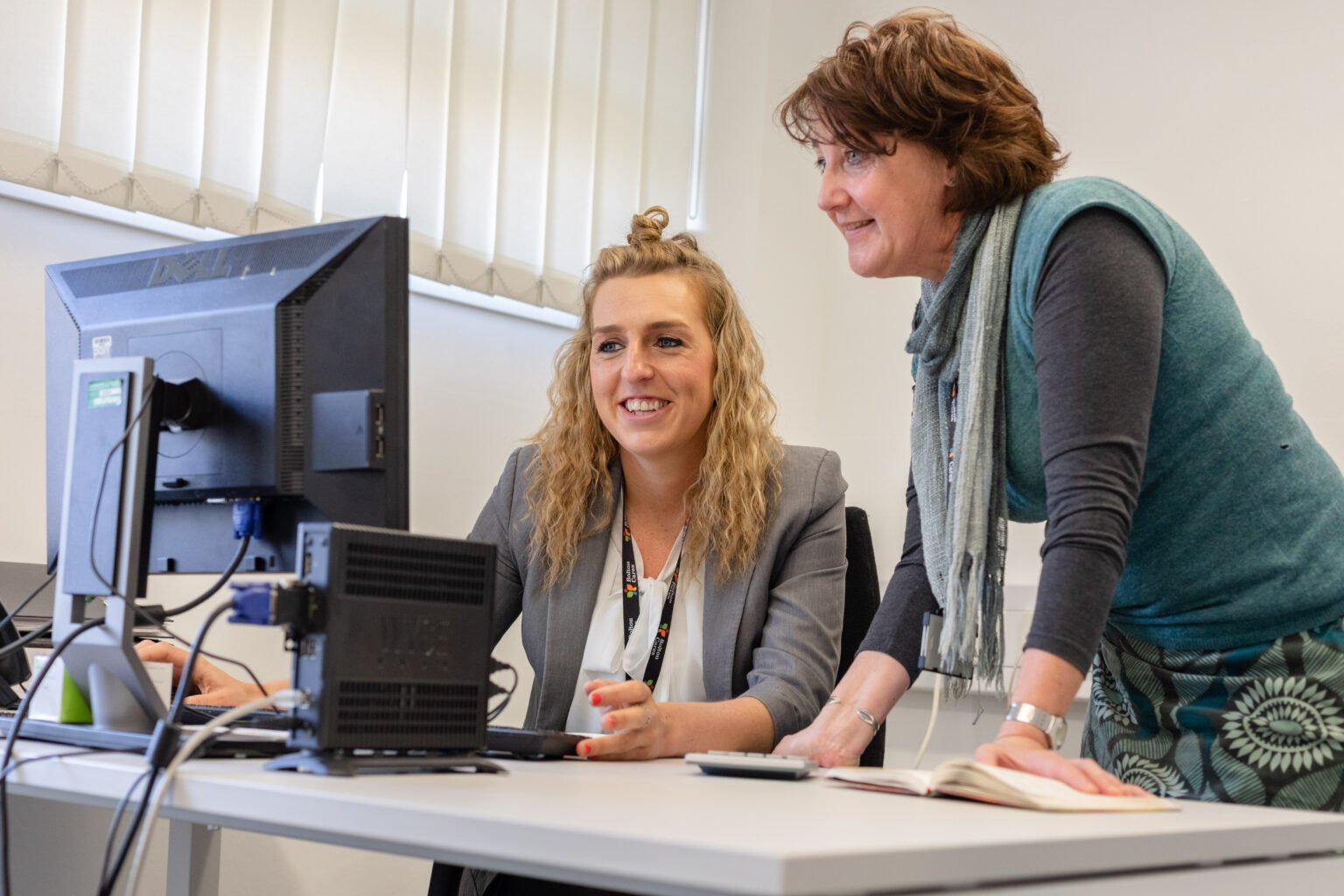 two women looking at a computer monitor, smiling as they work