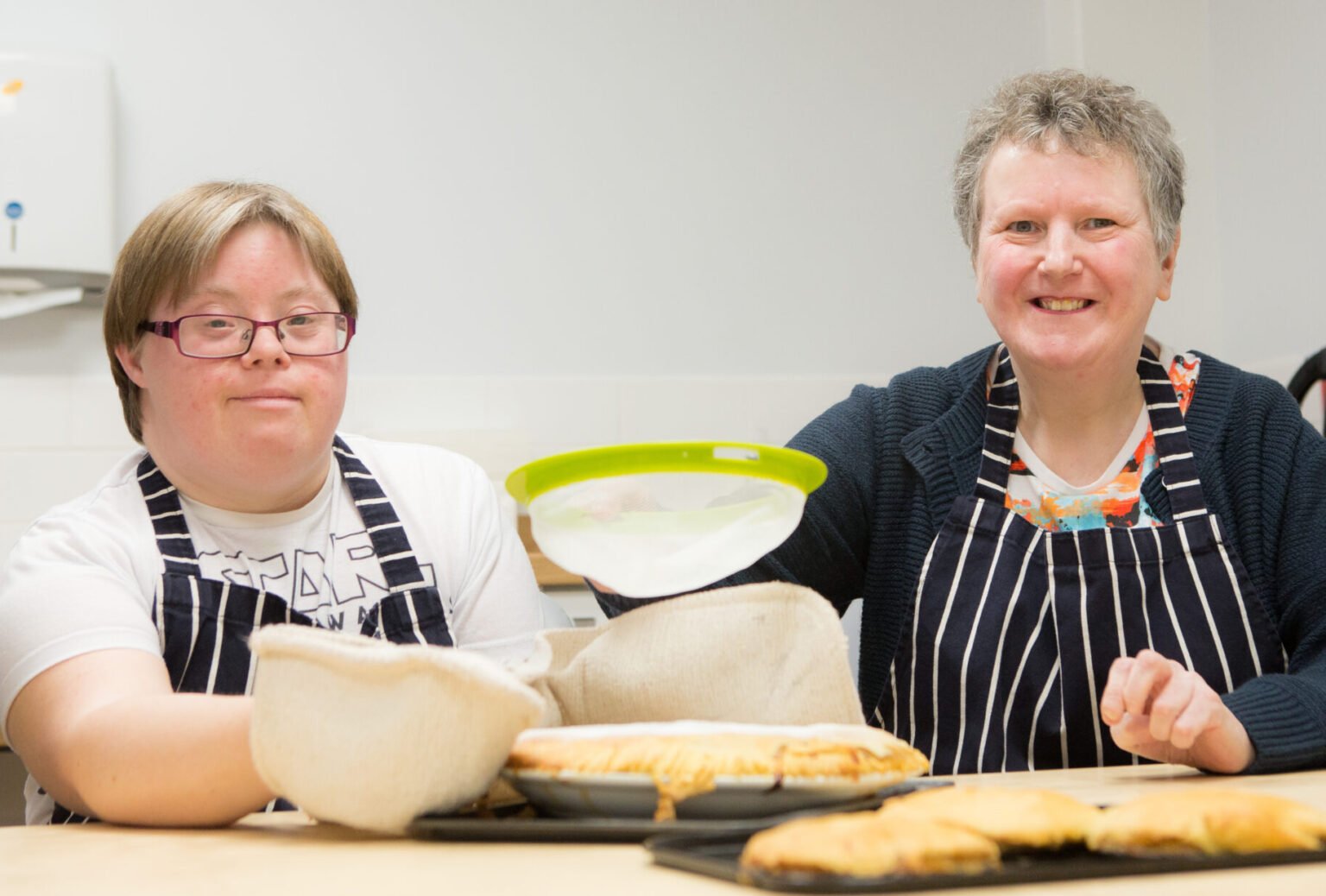 A woman and her carer, baking and smiling at the camara