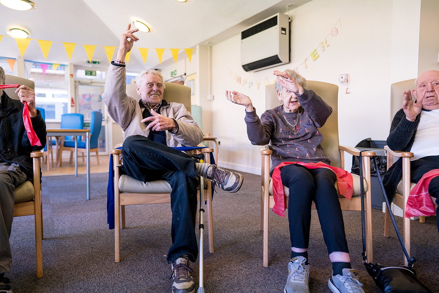 Elderly people sat in a circle waving their arms as they sing along to a song together