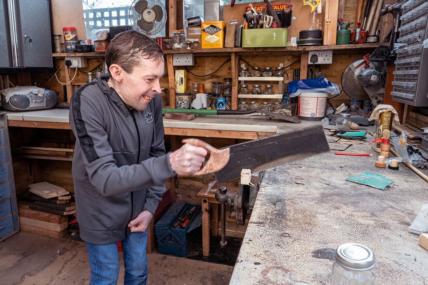 A young man in a woodworking garage, using a saw