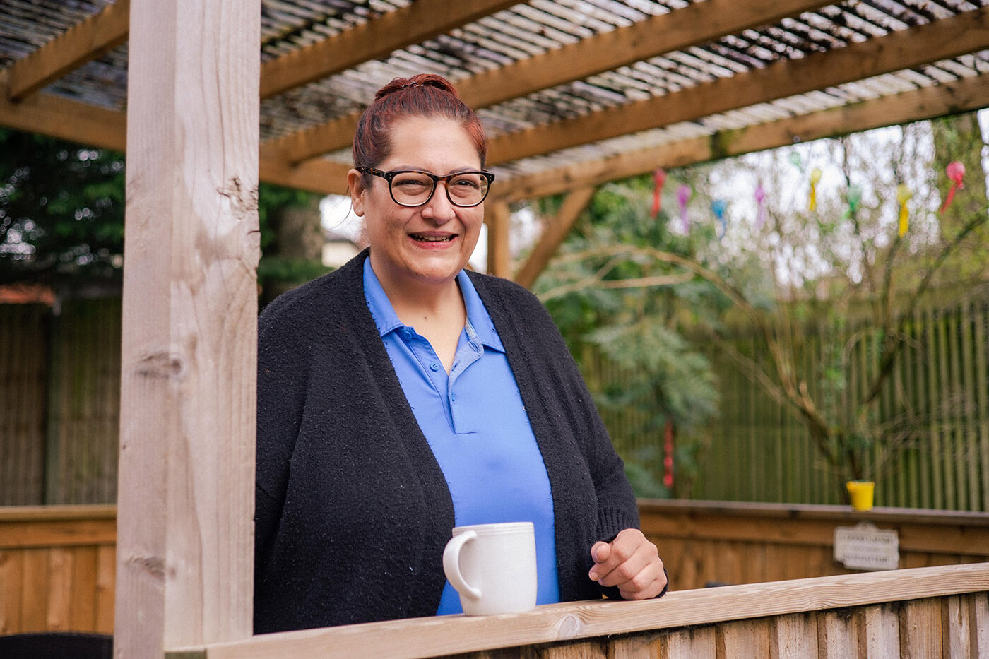 member of staff standing in the garden with a cup of tea, she's smiling at the camera