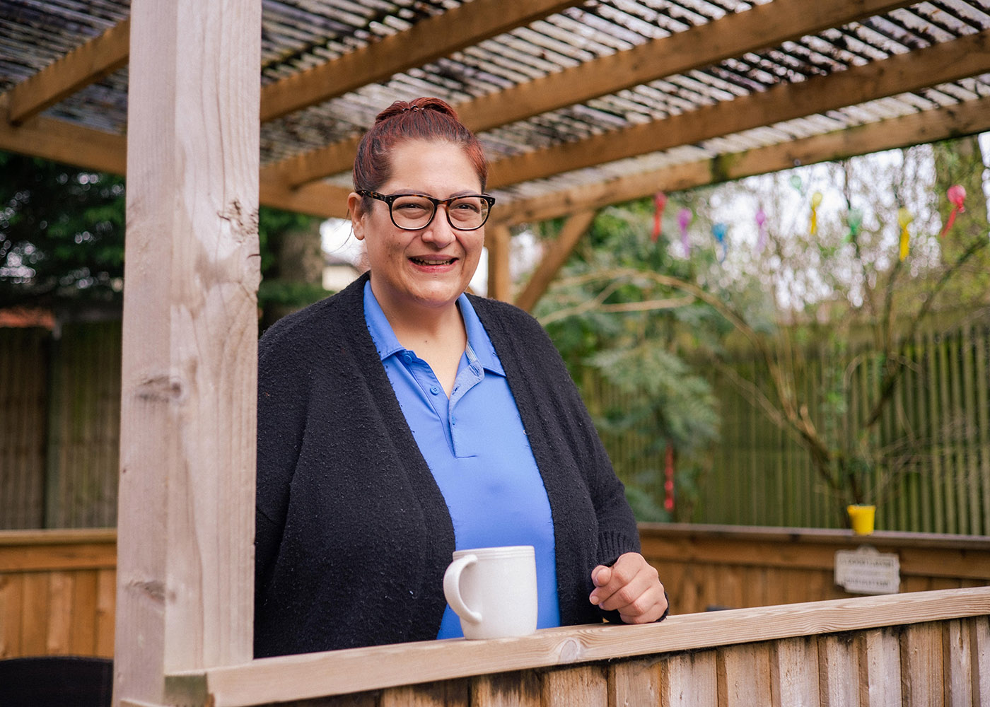 member of staff standing in the garden with a cup of tea, she's smiling at the camera