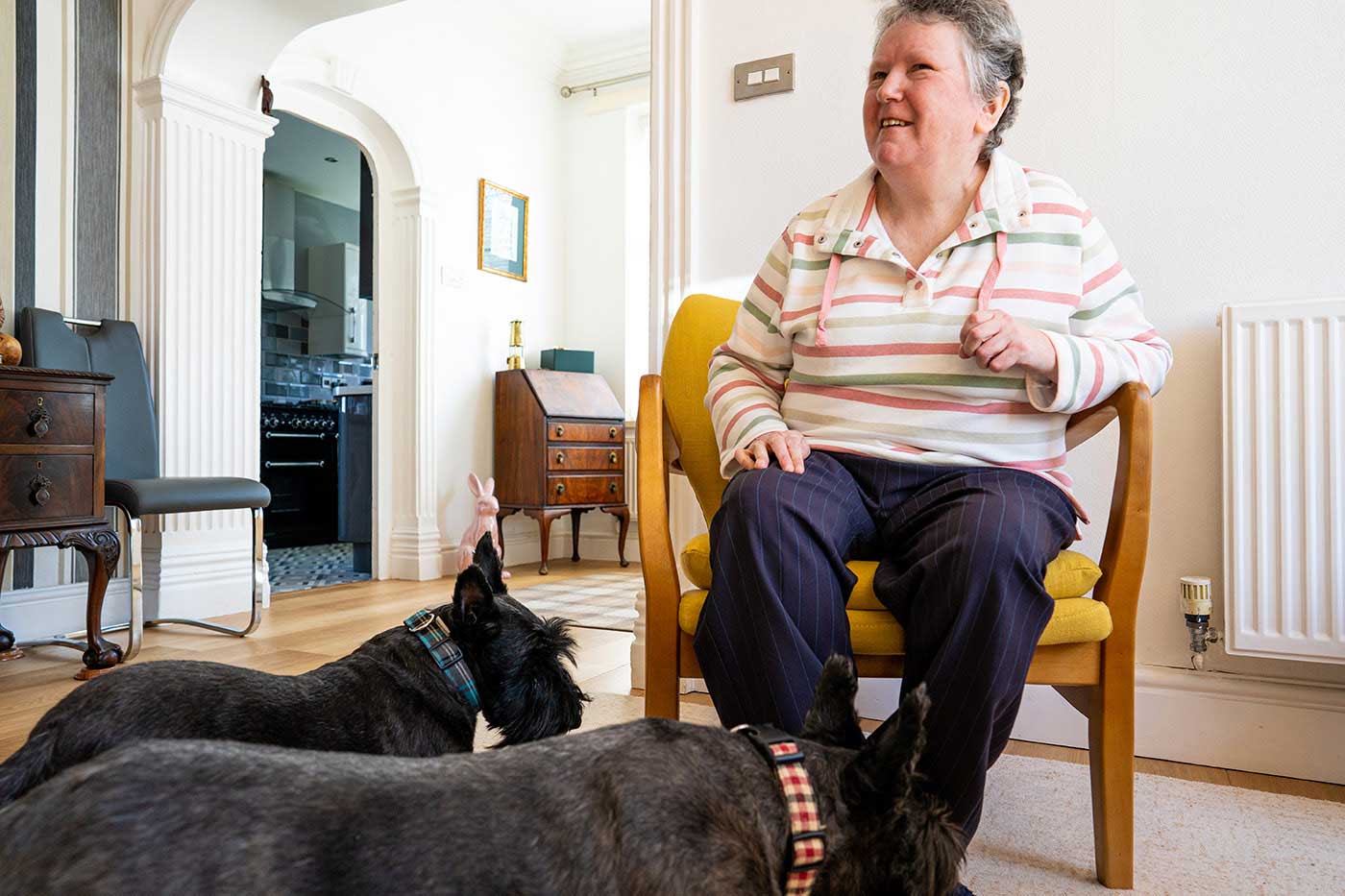 lady sat in her living room, she's smiling with her dogs at her feet