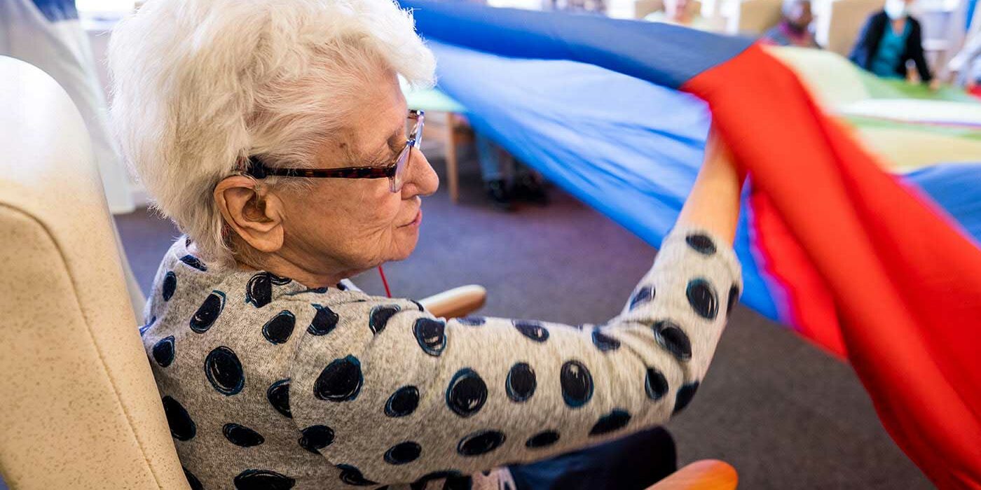 An older lady holding a parachute, playing a game with others