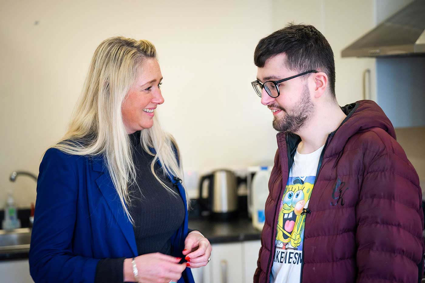 Joshua and one of his carers having a conversation, they are laughing in his kitchen