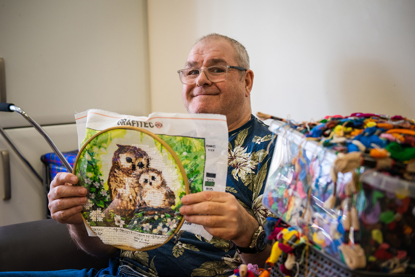 A man smiling at the camera holding up his needlepoint project